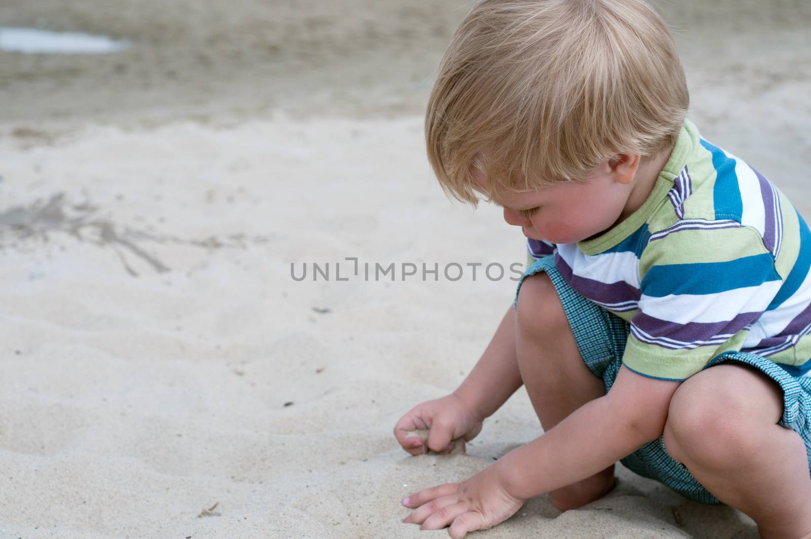 Little toddler boy playind with sand on the beach