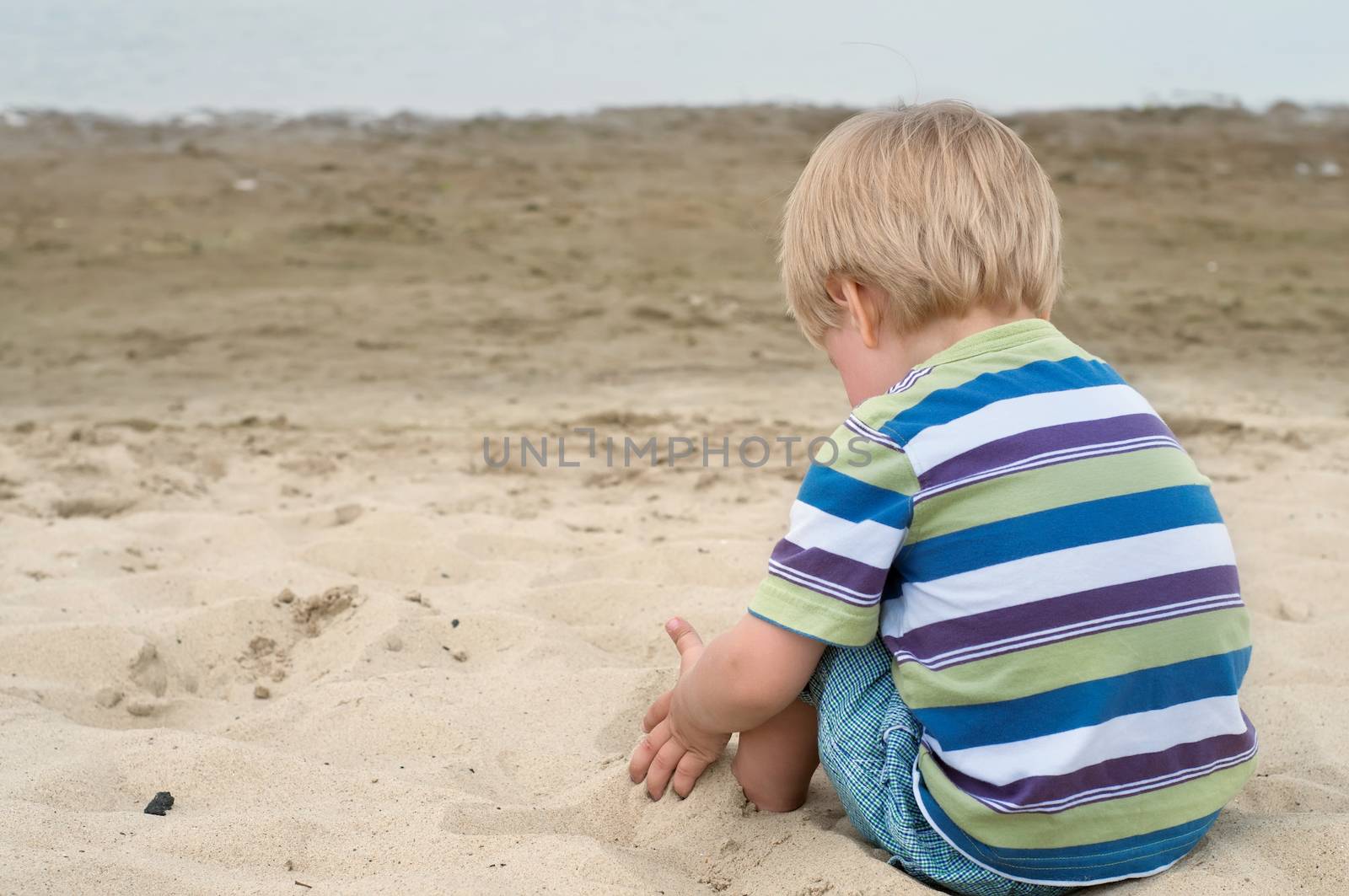 Little toddler boy sitting back on sandy beach by anytka