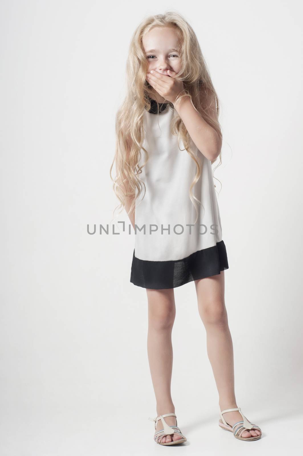 Little girl in white dress covers her mouth with her palm