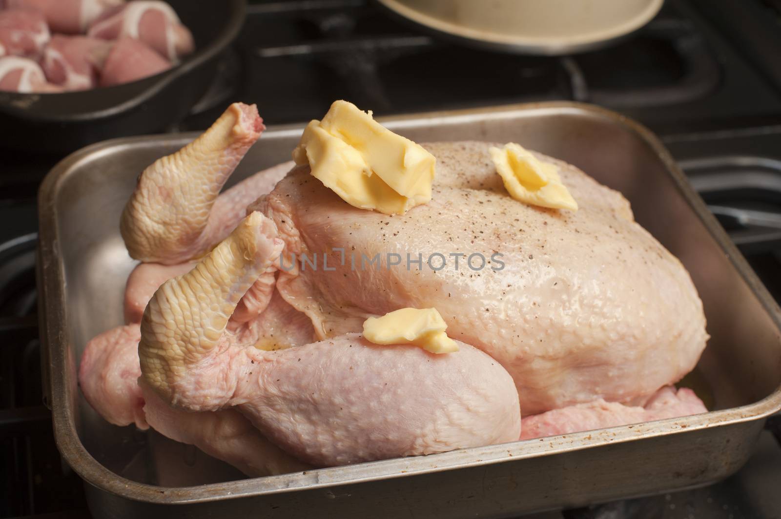 Uncooked seasoned turkey topped with dollops of butter in a roasting pan or oven dish waiting to be placed in the oven for roasting