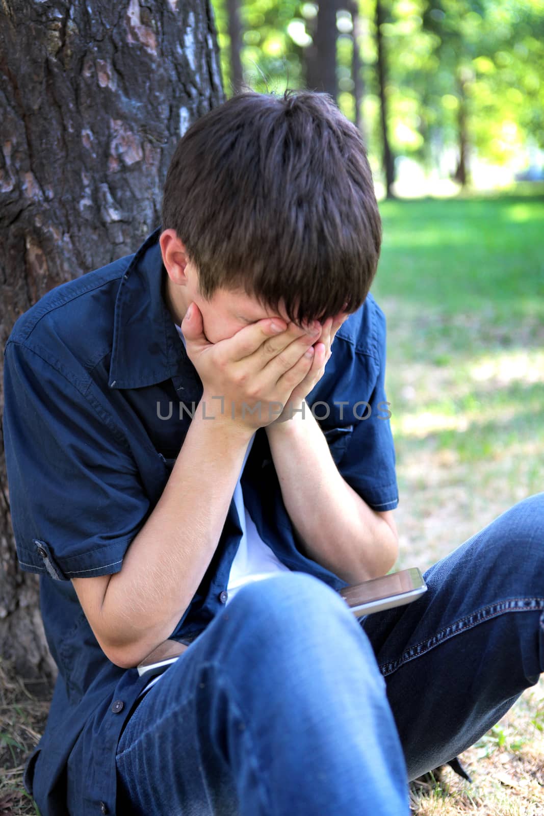 Sorrowful Teenager sitting in the Park near the Tree