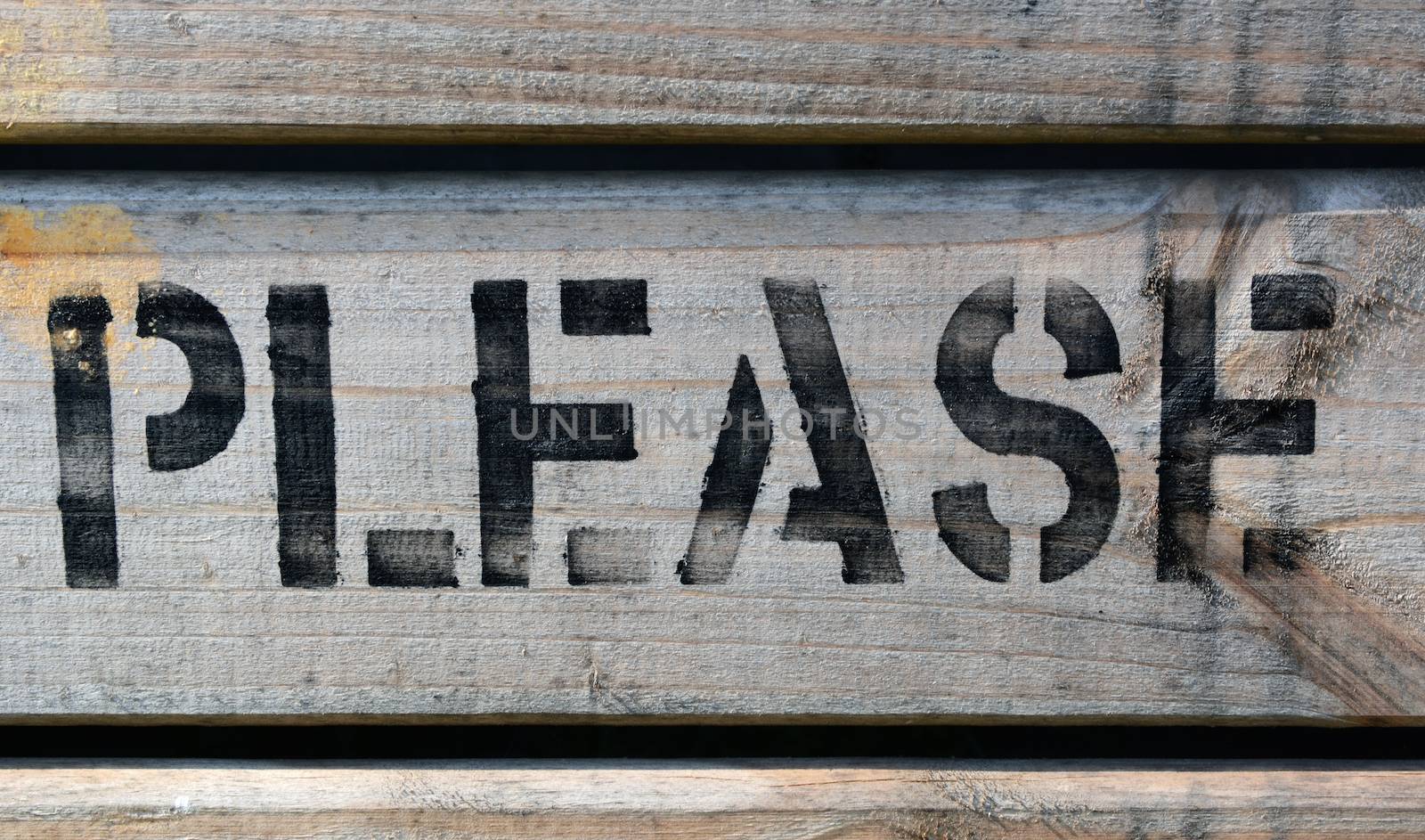 The word PLEASE stencilled in block capitals with black paint on wood
