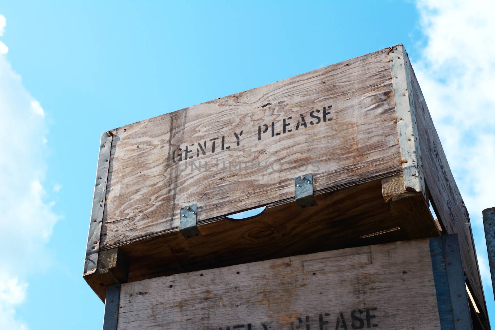 Wooden fruit boxes stacked high against a blue sky, labelled with the words GENTLY PLEASE.