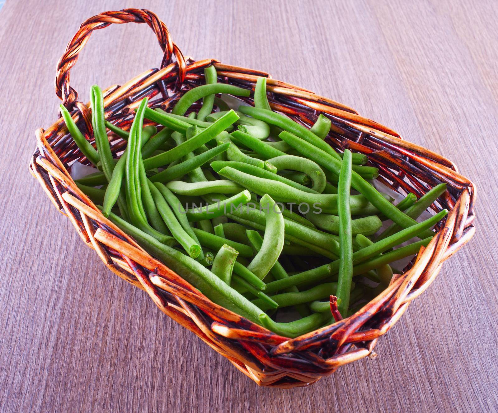 Grean beans in a small basket, over wooden table