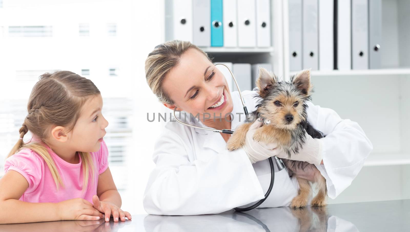 Veterinarian examining puppy with girl by Wavebreakmedia