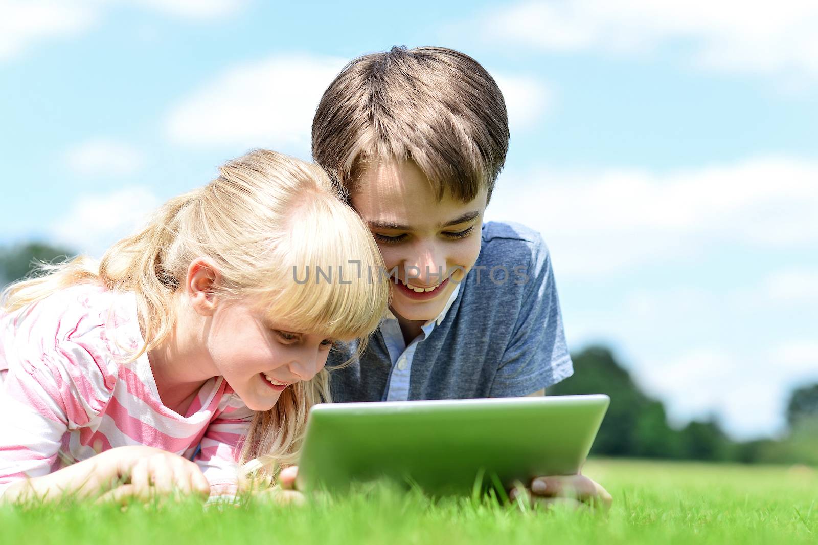 Two children lying down and using tablet pc by stockyimages