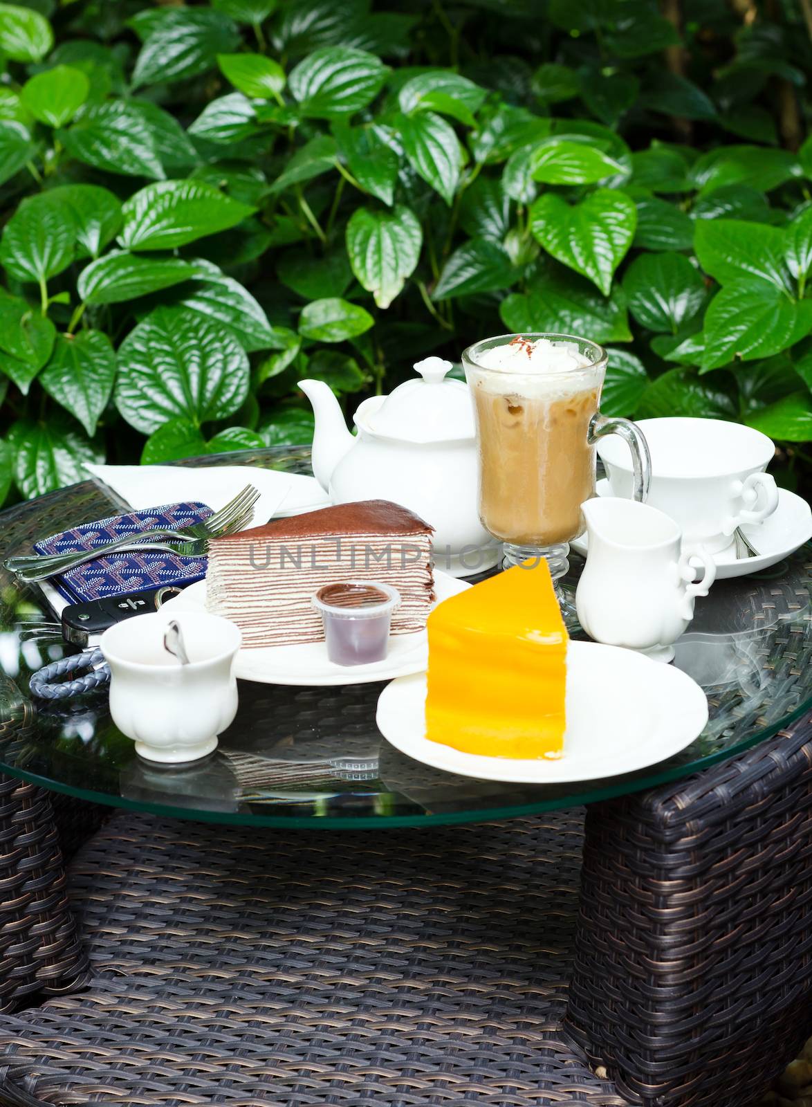 Coffee, tea, chocolate crape cake and orange cake on table in garden