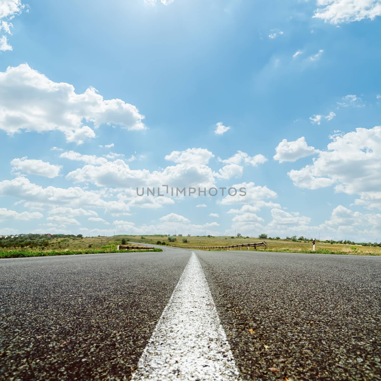 white line on asphalt road under sky with sun and clouds by mycola