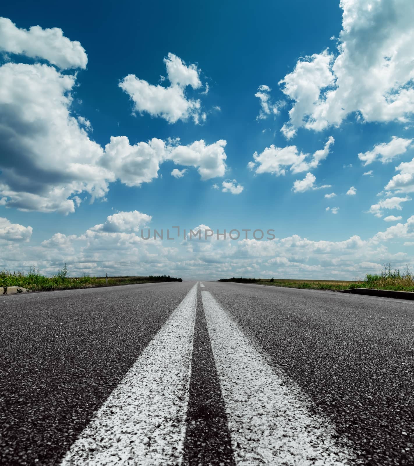 two white lines on black road and dramatic sky with clouds over  by mycola