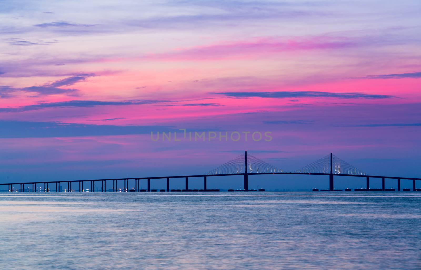 Panorama of bright sunrise lighting up the sky behind Sunshine Skyway Bridge from St Petersburg Florida across Tampa Bay.
