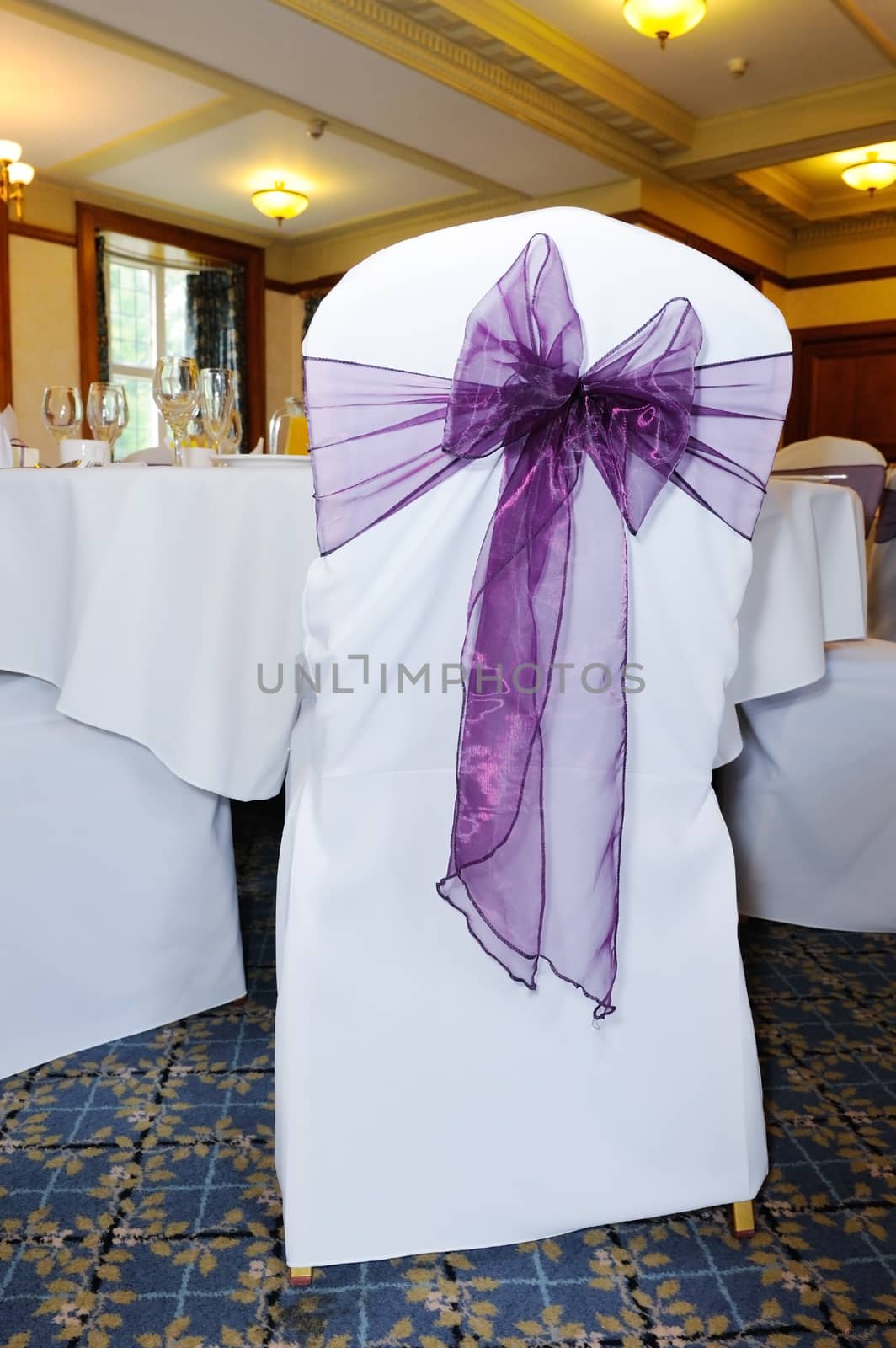 White chair at wedding reception decorated with purple ribbon tied in bow