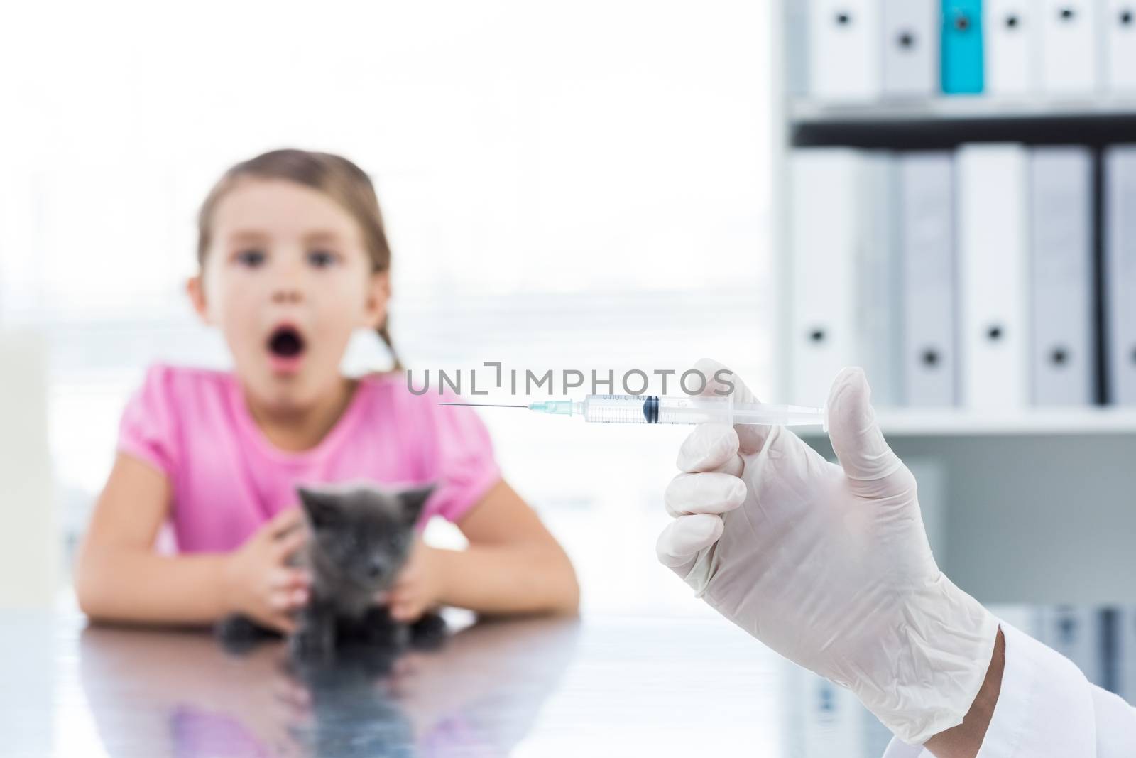 Vet holding syringe with socked girl holding kitten by Wavebreakmedia