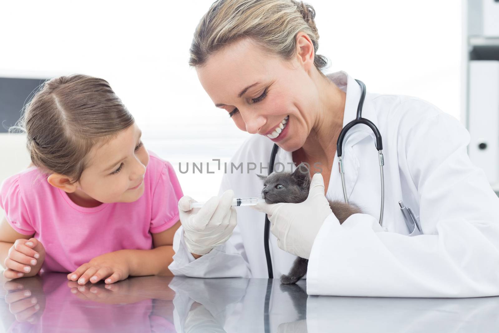 Female vet giving cat medicine through mouth with girl in clinic
