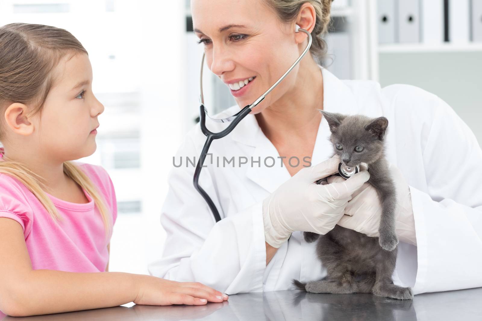 Female veterinarian examining kitten with girl in clinic
