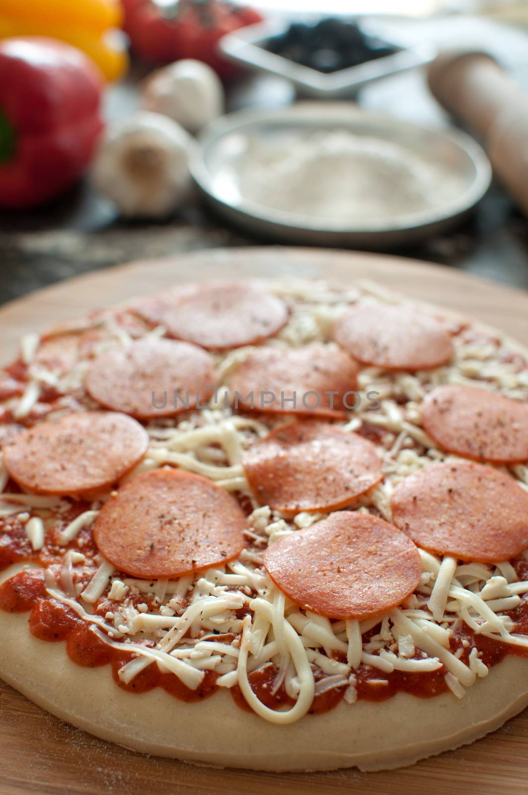 Fresh pizza dough with grated cheese and pepperoni on top of a chopping board  