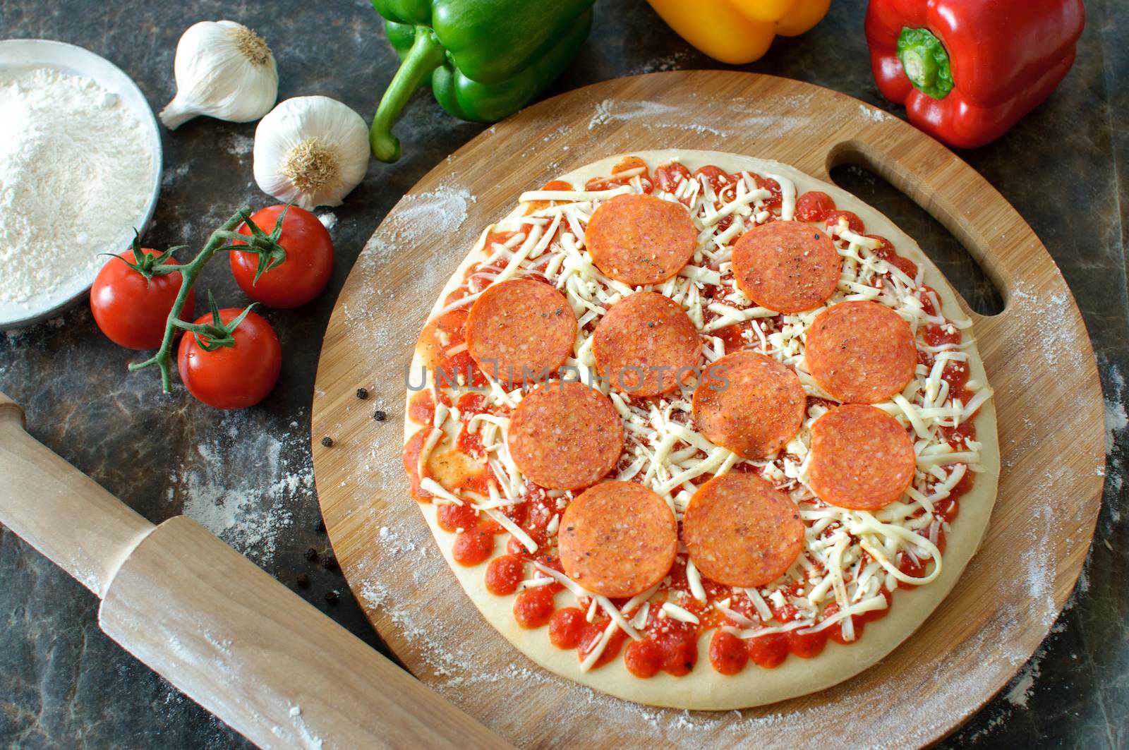 Pepperoni pizza preparation with rolling pin and fresh ingredients on the side