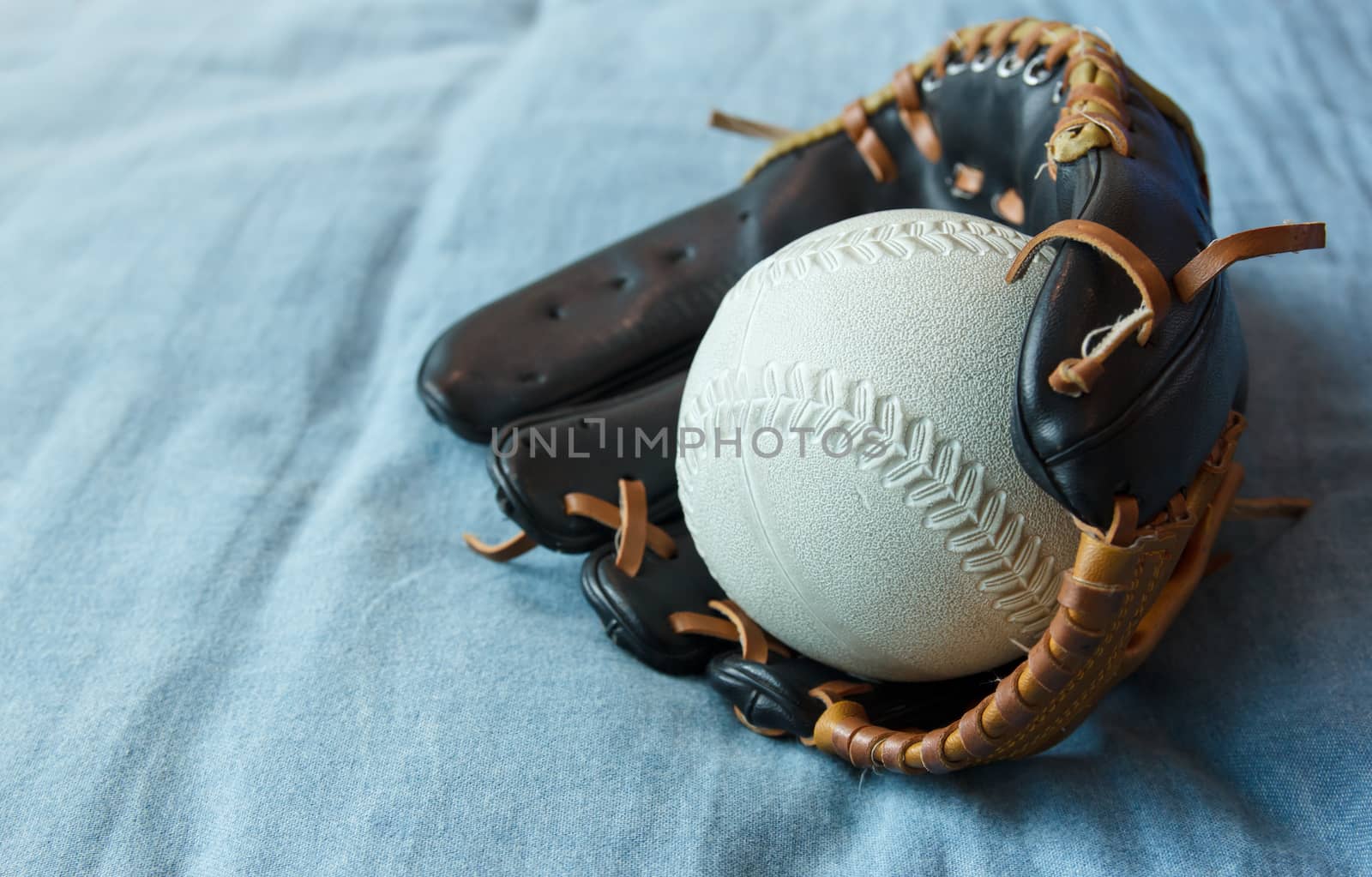 Old baseball in a glove on blue bed