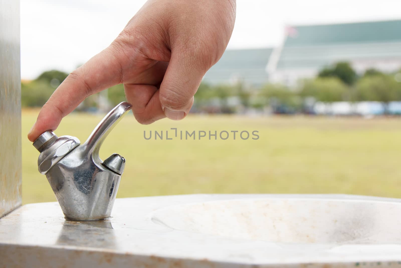 hand man push button of drinking water faucet at public park