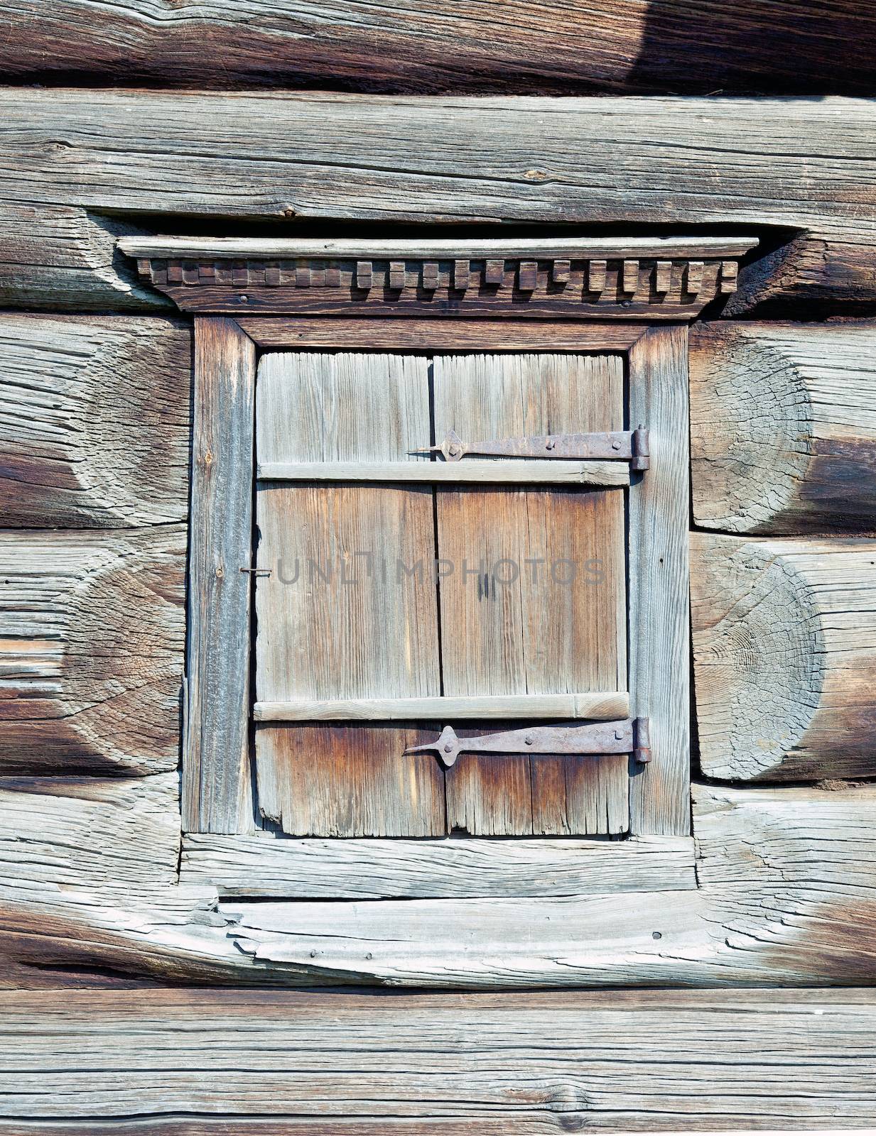 A small closed window in the wall of an old wooden house 