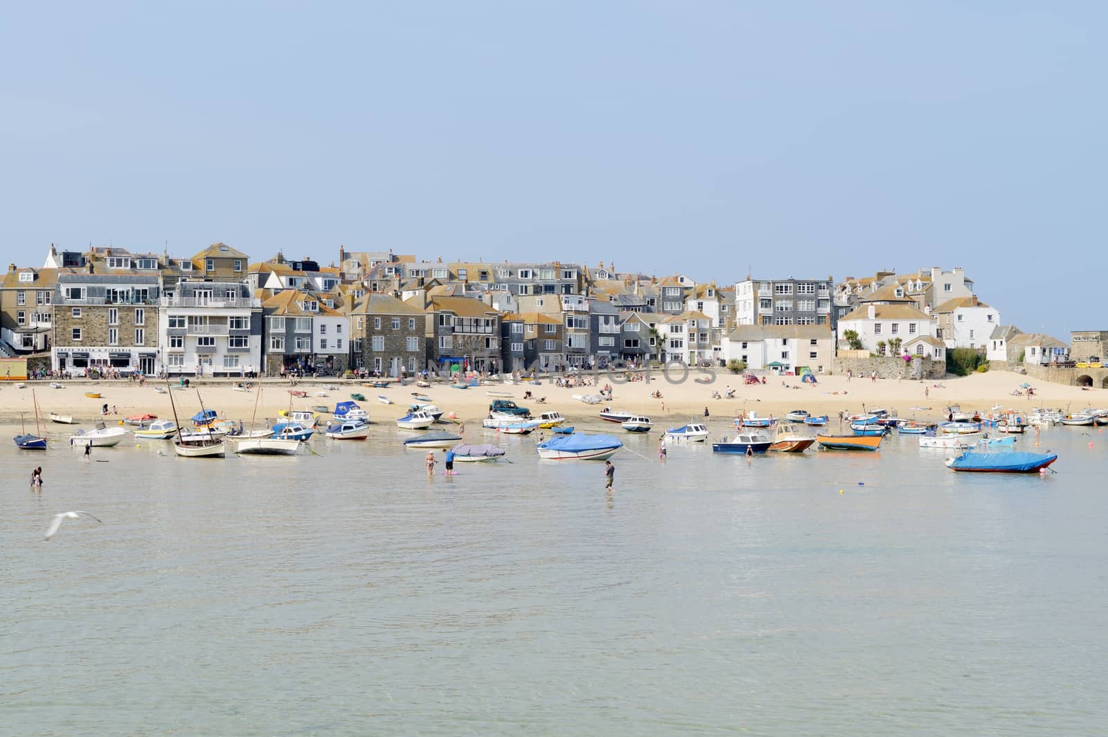 Sunny cornish beach in the summer with boats moored in the harbour