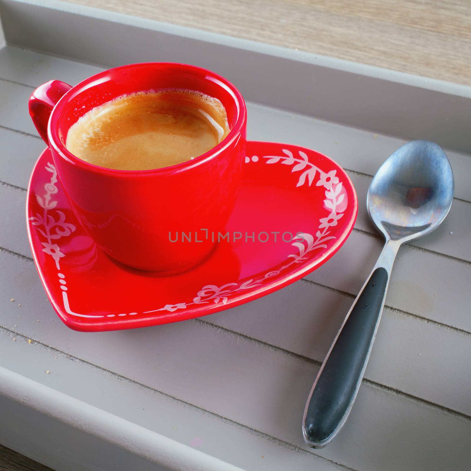 Red coffe cup with plate in shape of heart over a wooden tray