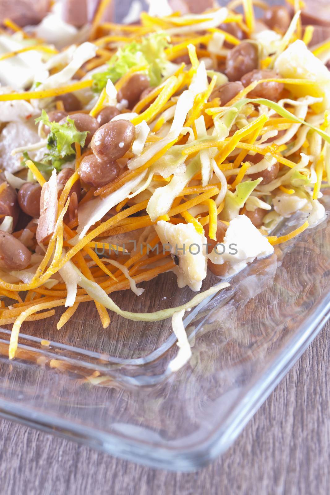 Salad with sausage, cheese, carrots, beans over glass plate