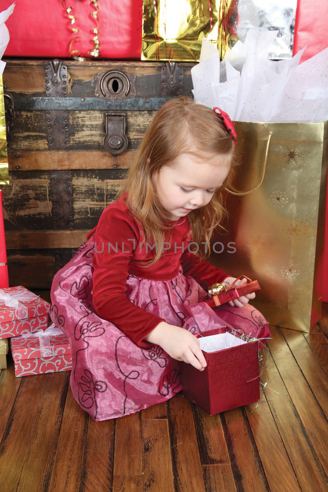 Little girl wearing a christmas dress looking at gifts