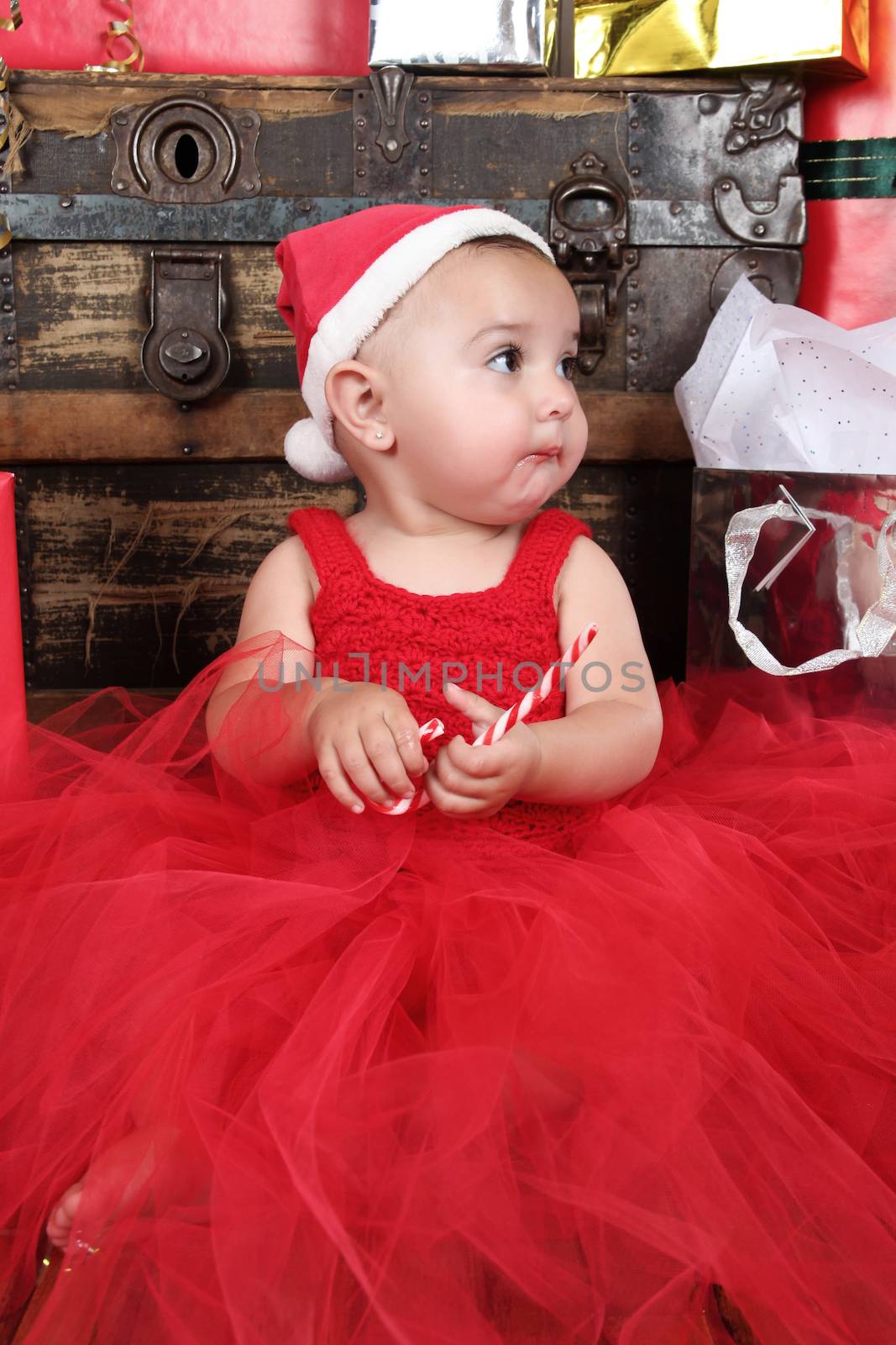 Brunette baby girl wearing a red christmas dress eating candy