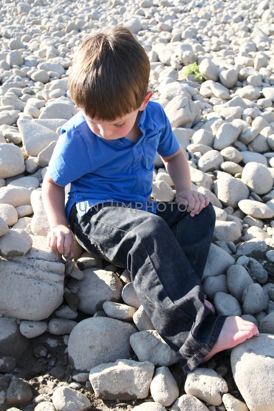 Younb boy sitting outside on pebble beach