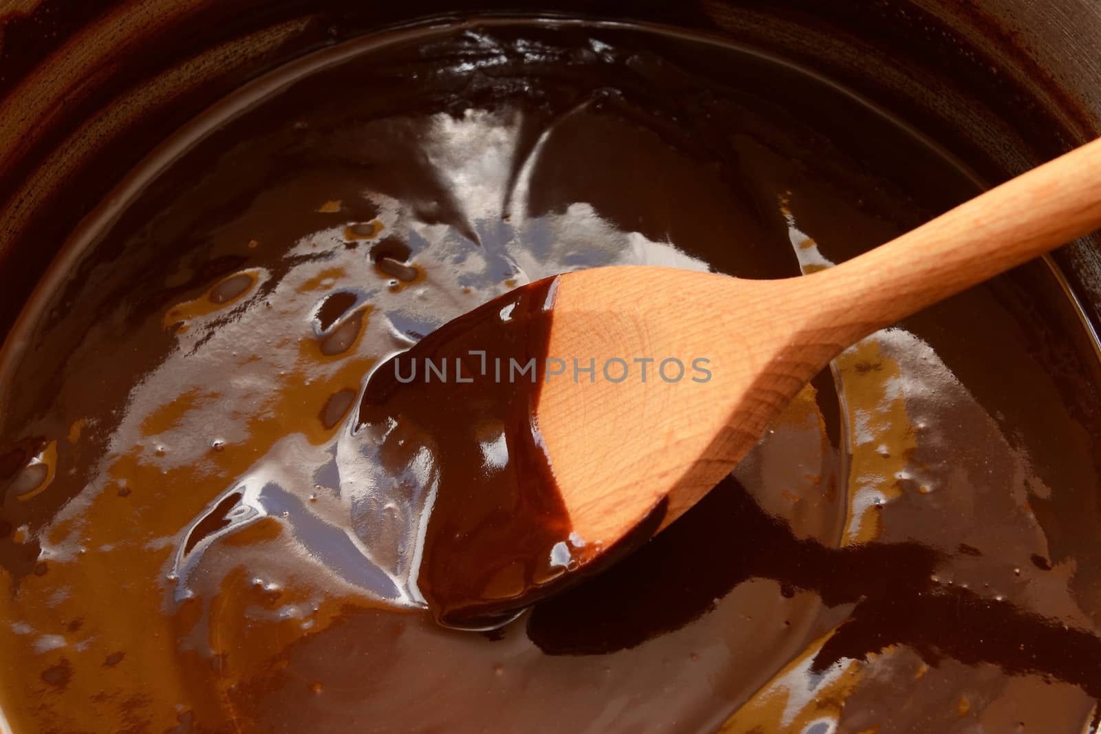 Melted dark chocolate in a saucepan, being stirred with a wooden spoon