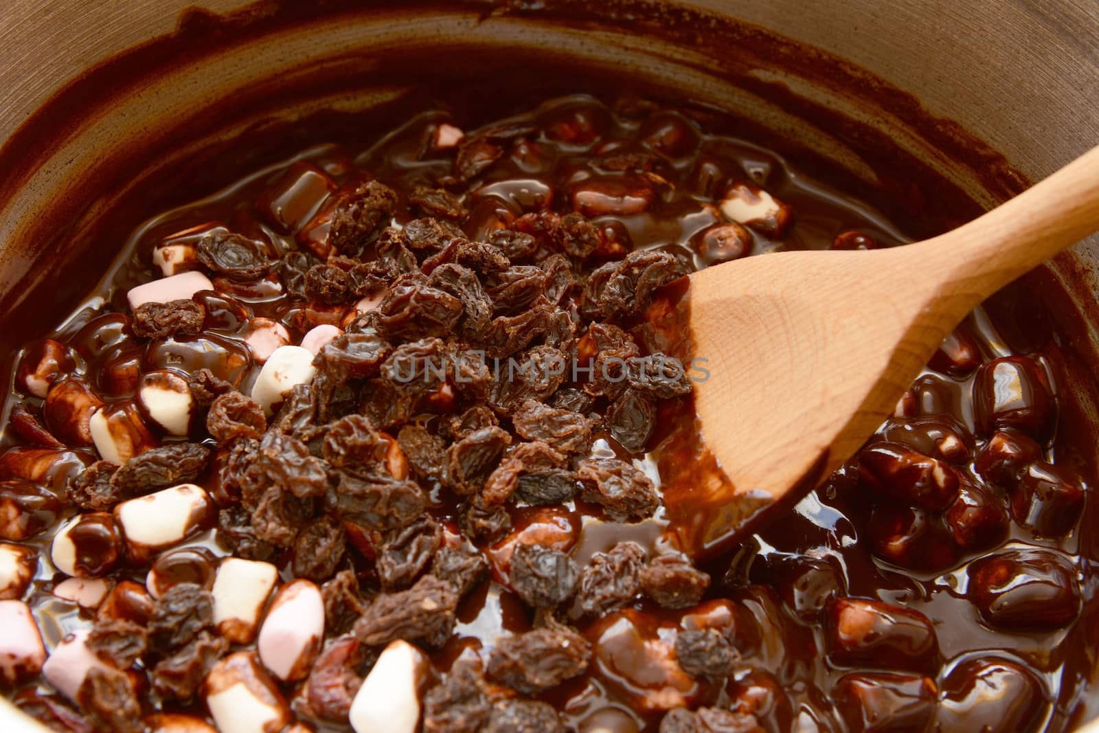 Mixing raisins with marshmallows and melted chocolate to make rocky road