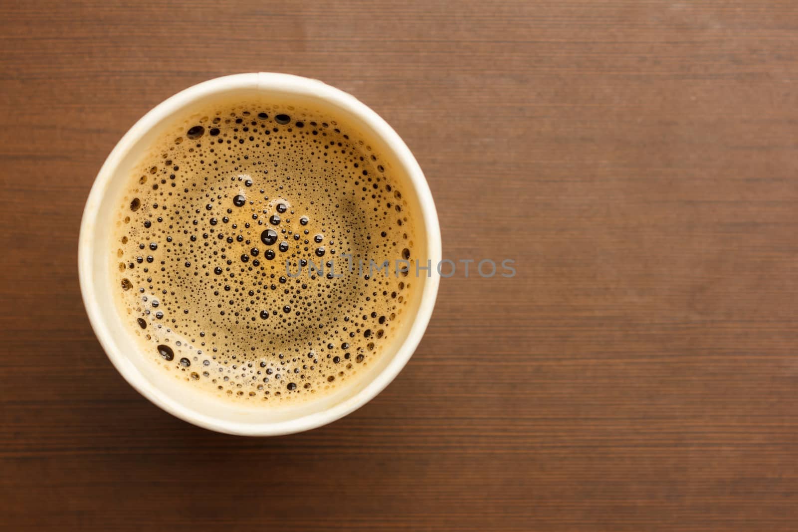 Top view of a paper cup of black coffee on wooden table