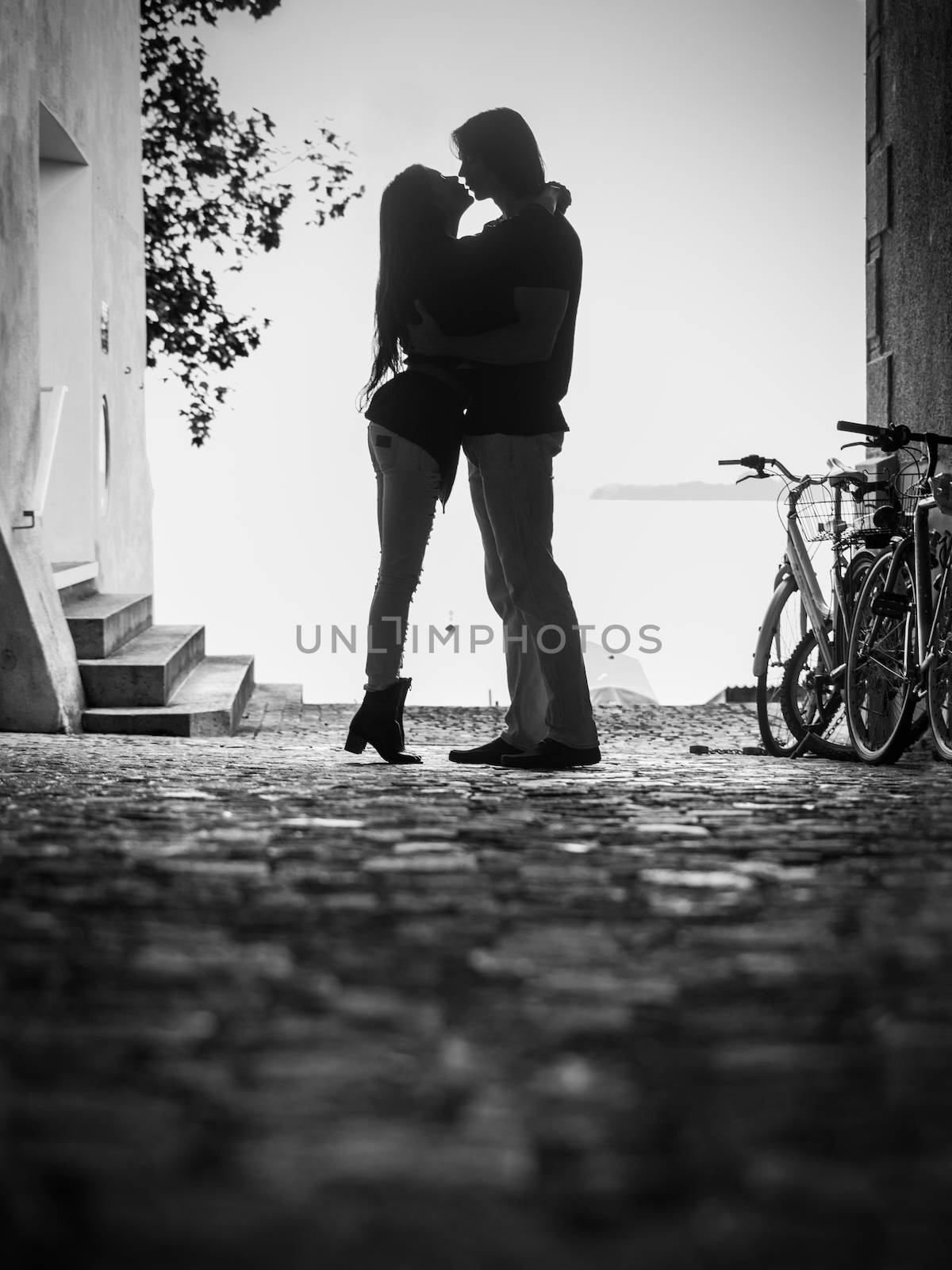 Photo of a young woman and man embracing and kissing in an alley.  Slight grain visible.
