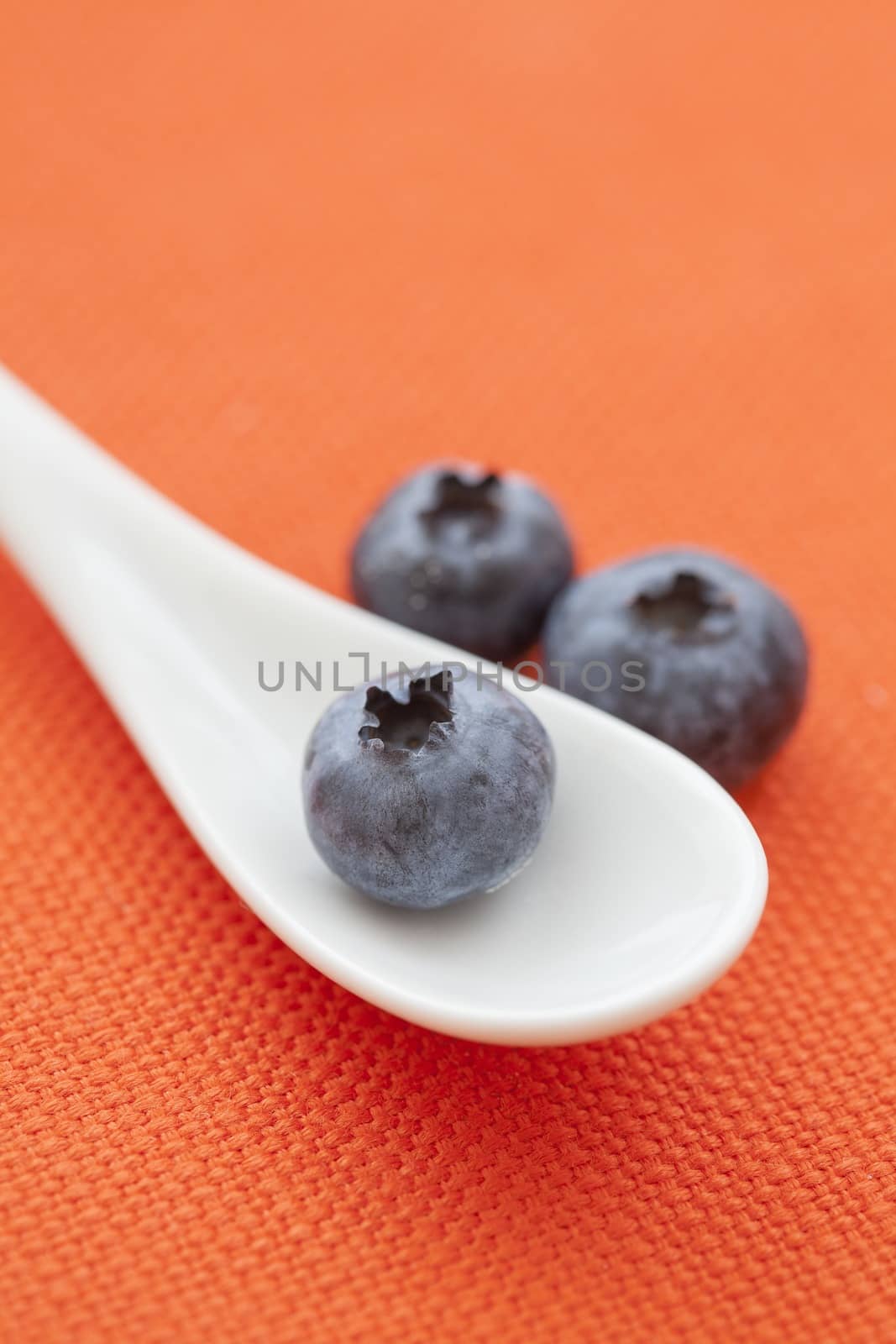 White spoon with blackberries, orange background.