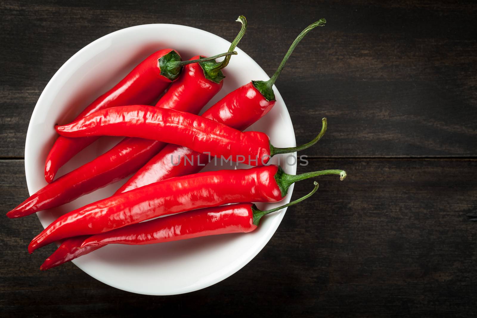 Red hot chili peppers on white plate on table background. Copy space. Top view