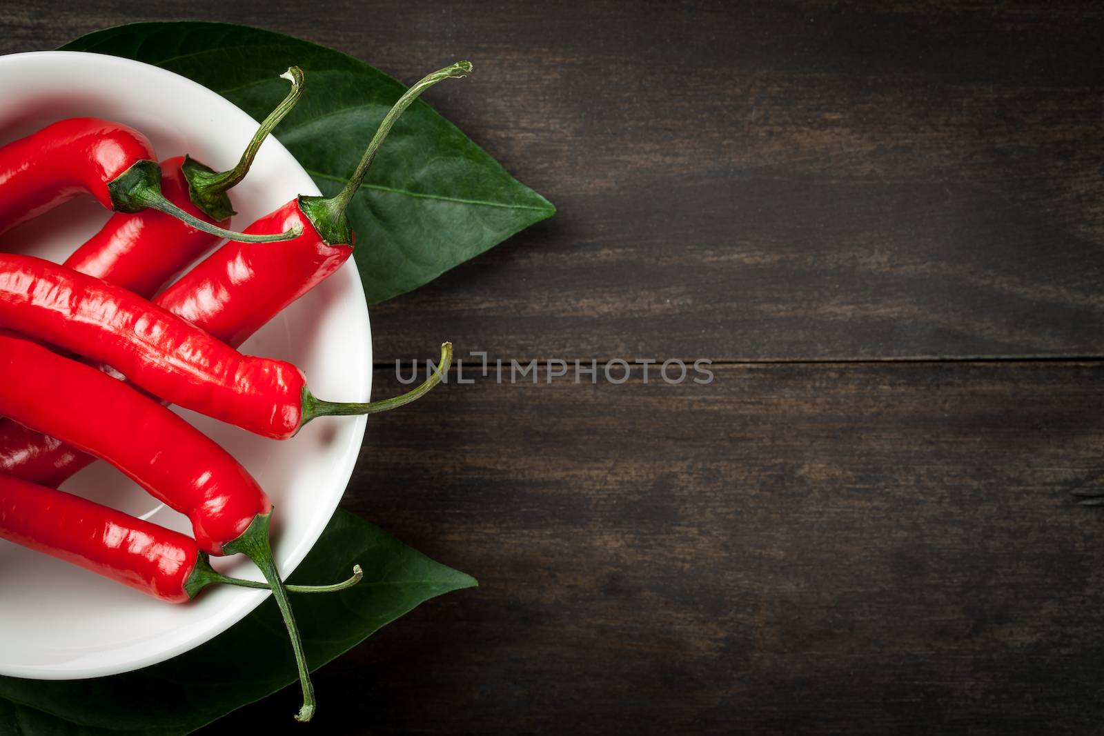 Hot chili peppers on white plate on wooden table background with copy space. Top view