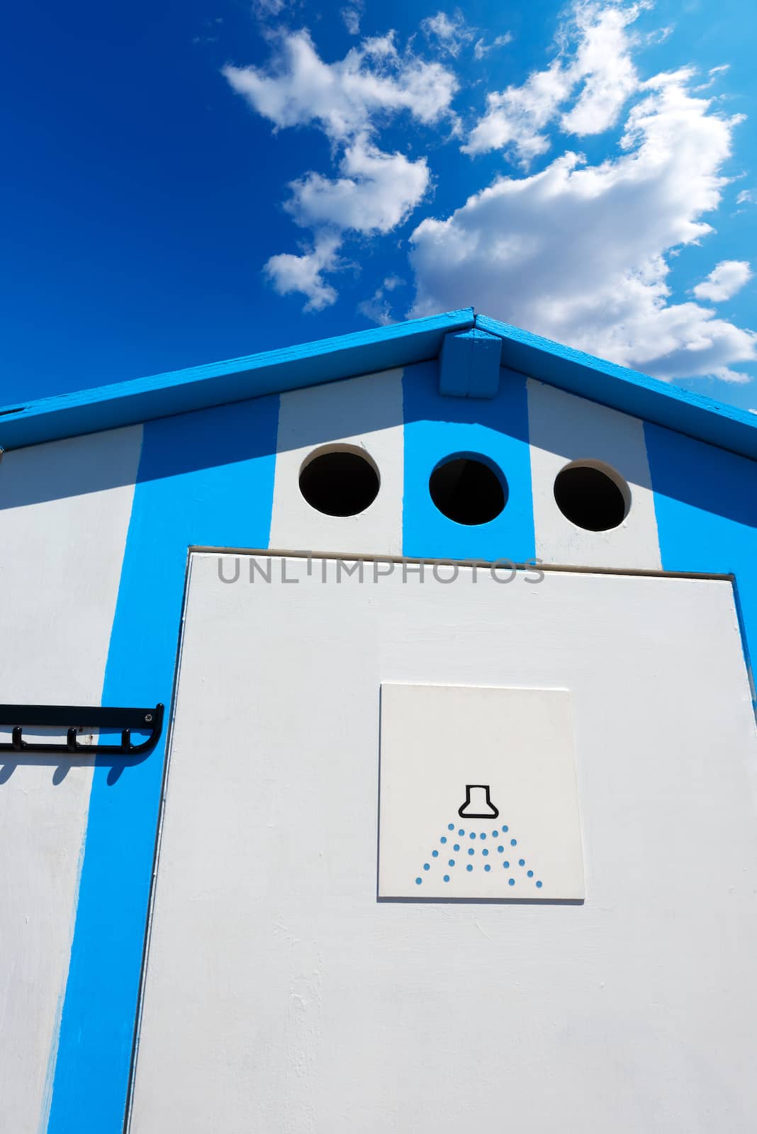 Detail of a wooden beach hut with blue and white striped for shower on a blue sky with clouds