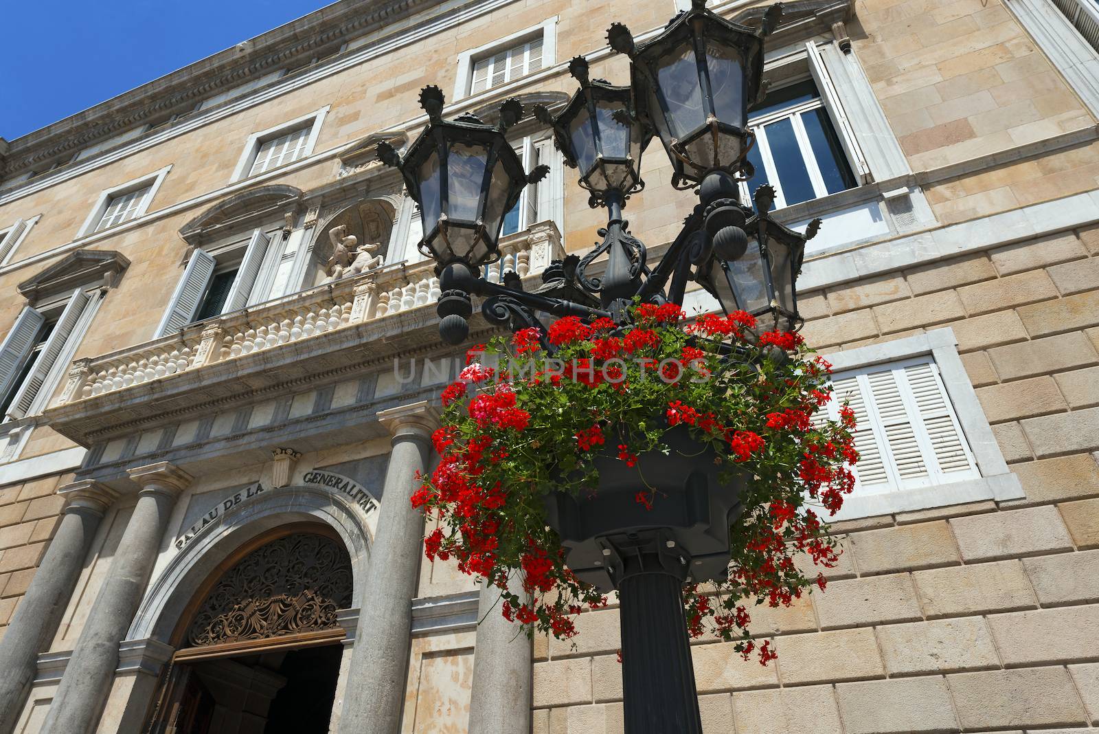 Red geraniums on a typical lamp post of Barcelona, Spain. In the background the Palau de la Generalitat de Catalunya (XV-XVII century)