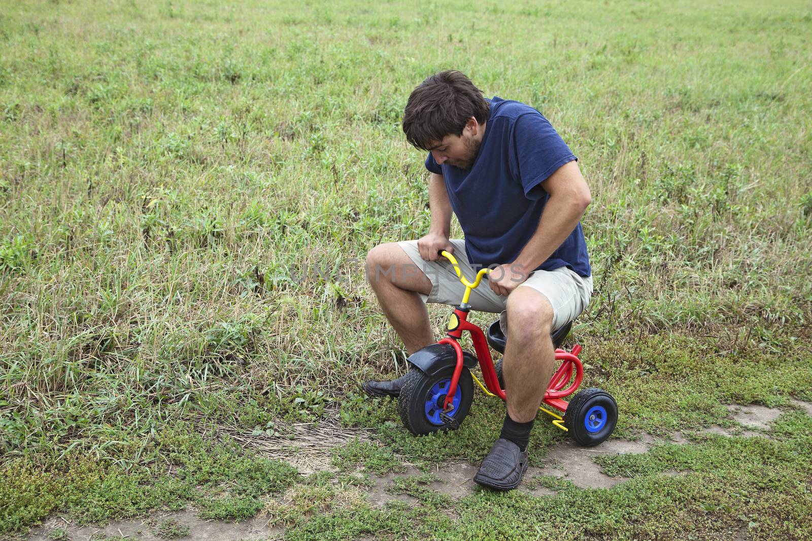 Adult man tying to ride on a small tricycle