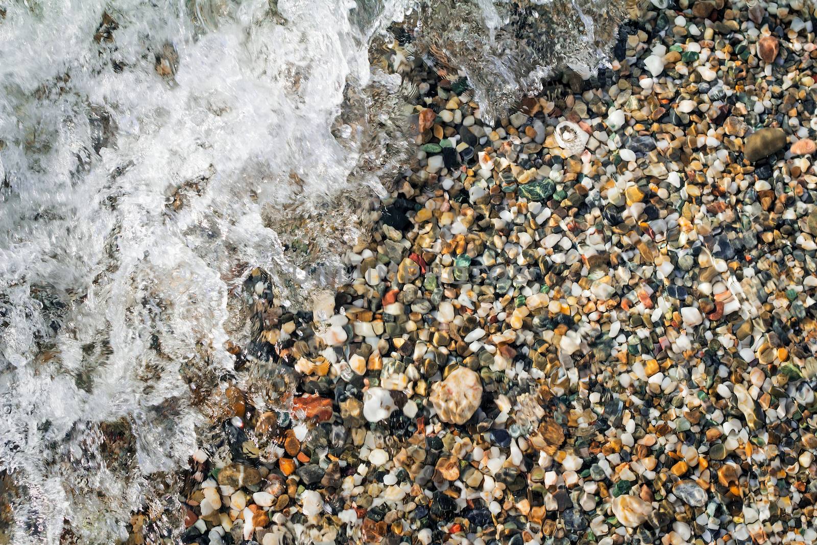 Small multi-colored sea stones on the beach, covered with transparent sea water.