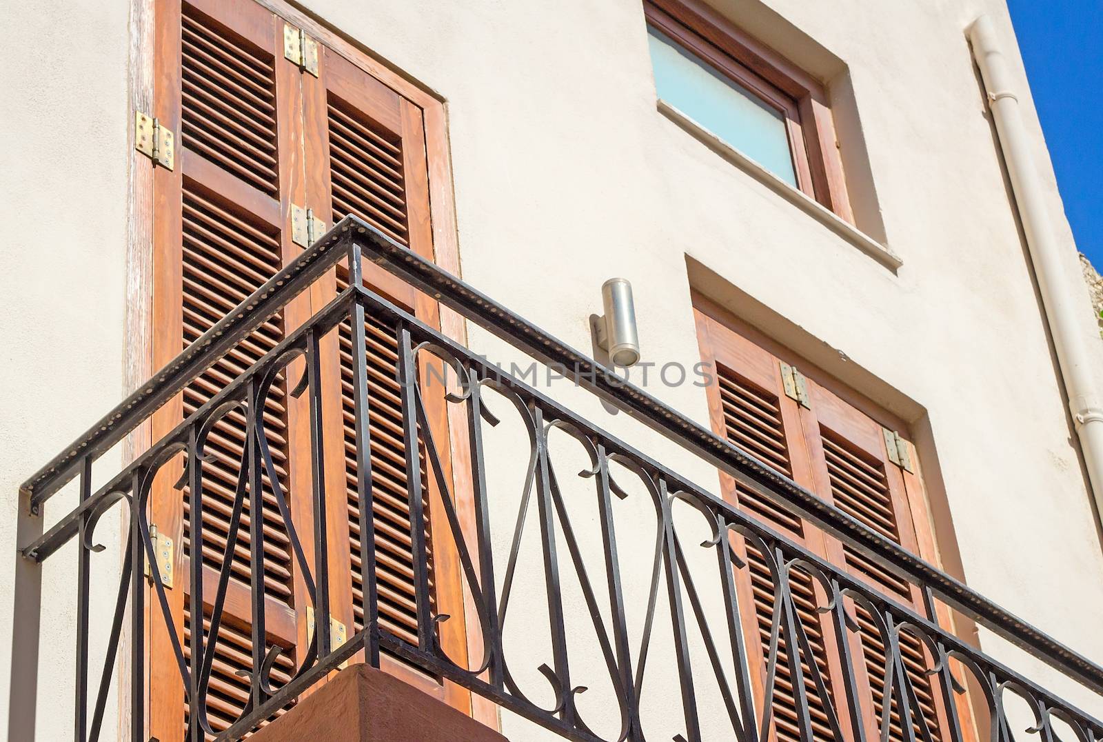 Fragment of a facade of the old house on the coast of the island of Crete with a balcony and ancient wooden blinds from the sun.