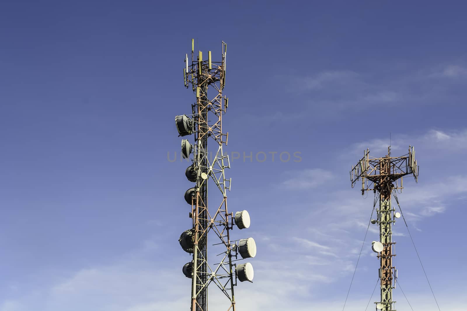 Two communication towers shot against blue sky.