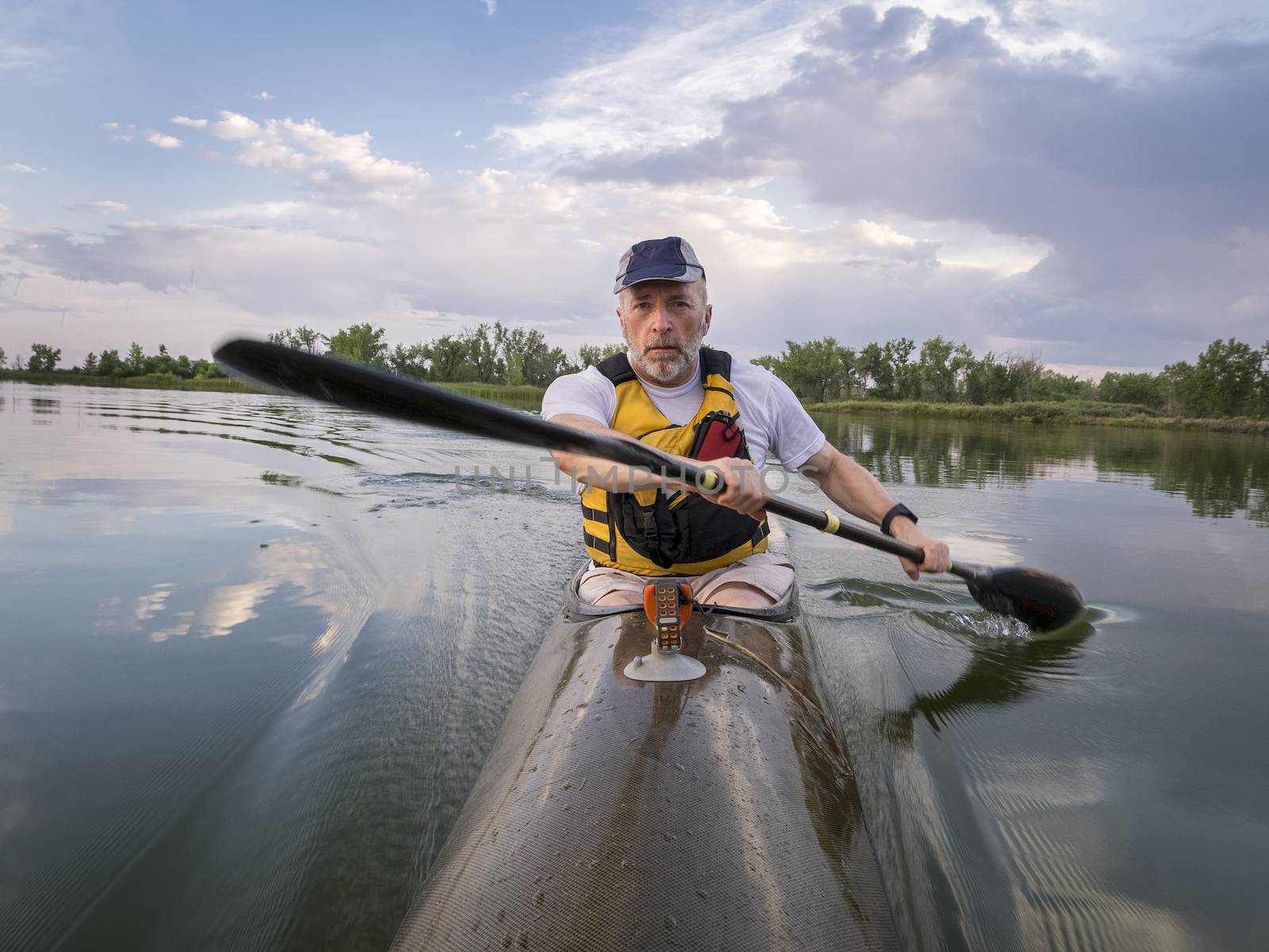 senior male is  paddling racing sea kayak  on a calm lake with storm clouds in background, Fort Collins, Colorado