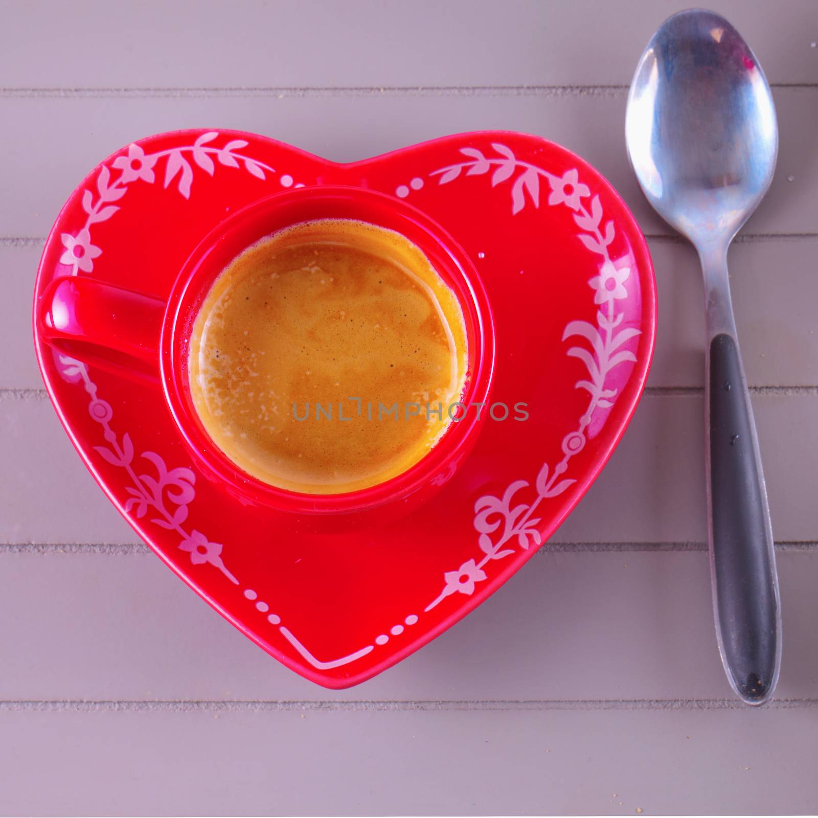 Red coffe cup with plate in shape of heart over a wooden tray