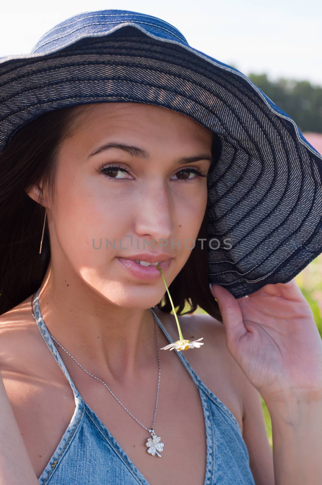 Woman in denim hat with chamomile in mouth
