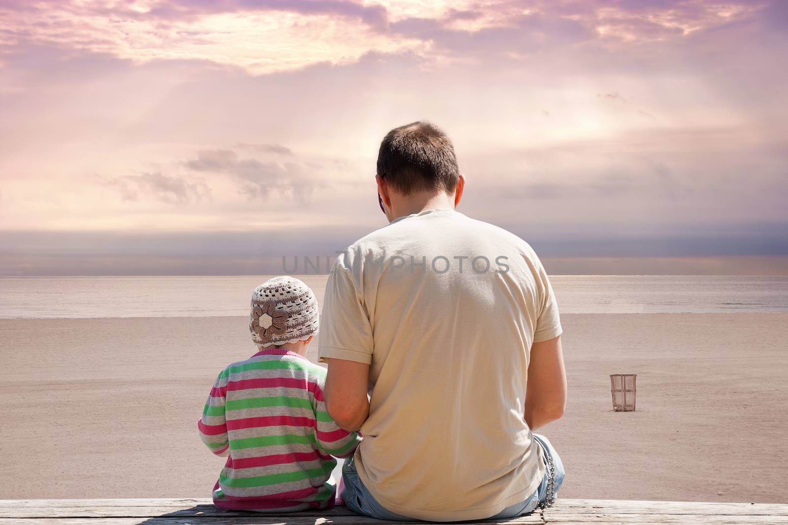 Father and daughter sitting on bench on empty beach at sunset with dramatic atmospheric clouds. Miami Beach Florida, USA.