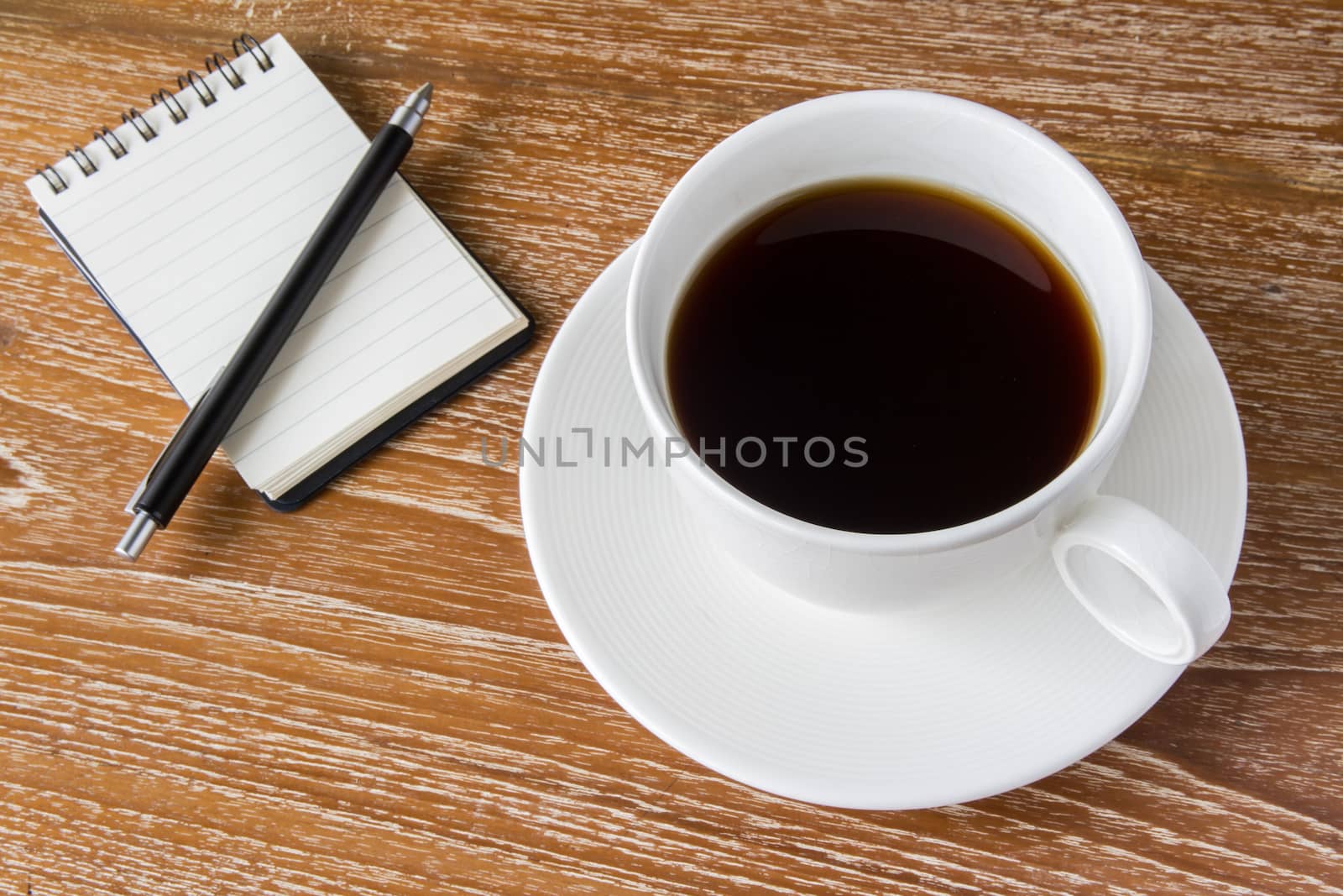 White cup of coffee on wooden table with notebook