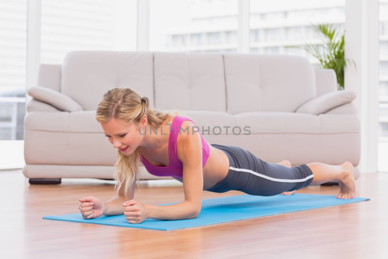 Fit blonde in plank position on exercise mat at home in the living room