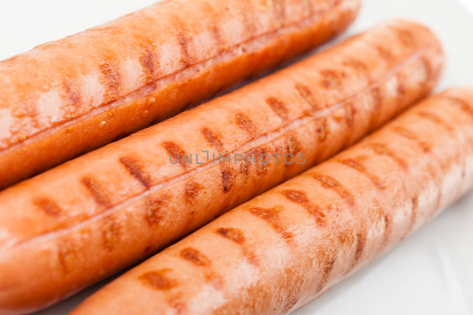 Three delicious wurstel on a white plate over white background
