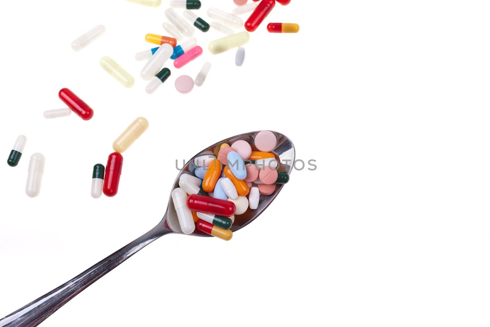 A lot of colored pills and tabs with a spoon over a white background